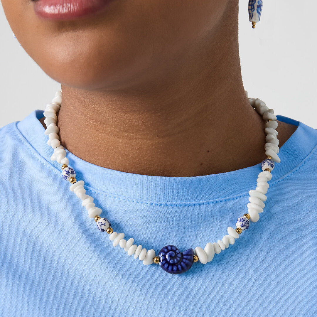 Collier composé de perles de pierre, de perles blanches ornées de fleurs bleues et d'un coquillage décoratif. Image